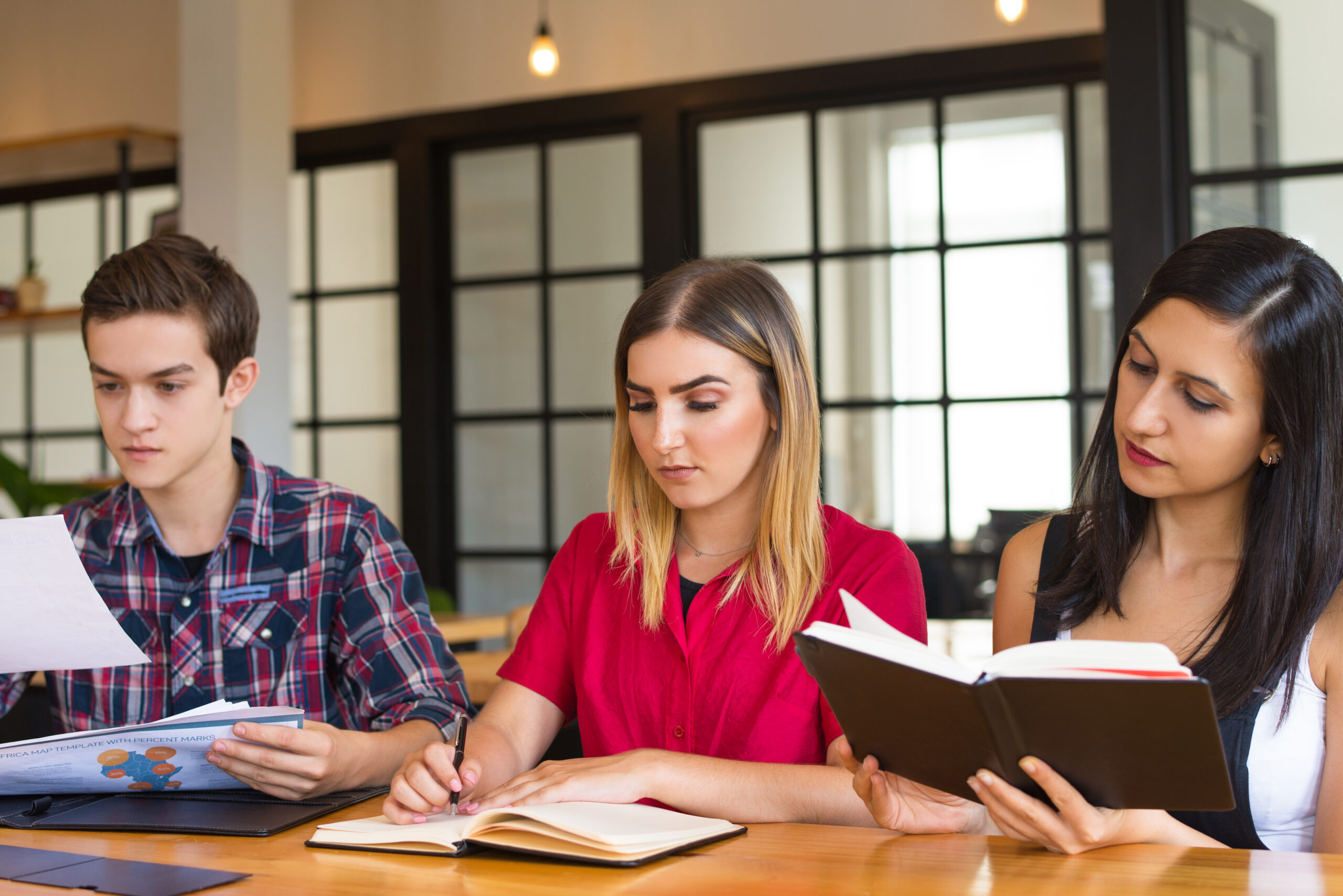 Portrait of three serious students studying in library Portrait of three serious students studying in library. Young Caucasian man working with papers and two women reading textbook. Education concept